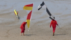 手拿旗帜的两人走在沙滩上